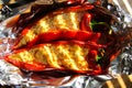 Close up of stuffed red paprika bell peppers with sheep feta cheese seasoned with spicy chili grilled in aluminium foil