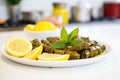 close-up of stuffed vine leaves on white plate, lemon slices on side