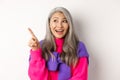 Close-up of stylish korean senior woman with grey hair looking and pointing upper left corner, showing promotion offer Royalty Free Stock Photo