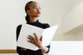 Close-up of successful African or black American business woman holding big white file and thinking