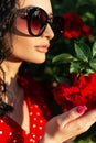 Close-up summer portrait of beautiful woman with fashionable sunglasses in red dress holding a rose in the garden in sunlight Royalty Free Stock Photo