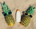 Close up summer two funny pineapple in colorful sunglasses and sunscreen skin bottle on a beach Royalty Free Stock Photo