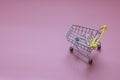 Close-up of supermarket grocery push cart, shopping trolley, and shopping cart with black wheels on pink background. Royalty Free Stock Photo