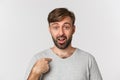 Close-up of surprised handsome man with beard, pointing at himself and looking confused, standing over white background Royalty Free Stock Photo