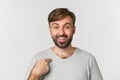 Close-up of surprised handsome man with beard, pointing at himself and smiling, standing over white background Royalty Free Stock Photo