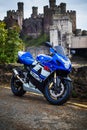 Close-up of a Suzuki motorcycle parked against a backdrop of Conwy castle in Wales