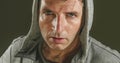 Close up sweaty face portrait of young attractive and fierce looking man wearing hoodie posing in aggressive and defiant attitude