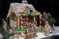 Close up of a sweet gingerbread family near snow-covered homemade gingerbread house on dark background