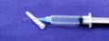 Close-up of a syringe with cannula and drop in front of dark blue background