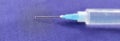 Close-up of a syringe with cannula and drop in front of dark blue background