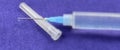 Close-up of a syringe with cannula and drop in front of dark blue background