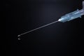 Close-up of a syringe with cannula and drop in front of dark blue background