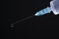 Close-up of a syringe with cannula and drop in front of dark blue background