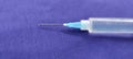 Close-up of a syringe with cannula and drop in front of dark blue background