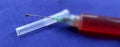 Close-up of a syringe with cannula and drop in front of dark blue background