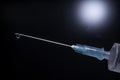 Close-up of a syringe with cannula and drop in front of dark blue background