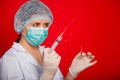 Close-up of a syringe with a stream of medicine from a needle in the hands of a female doctor on a red background.