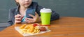 Close-up, on the table is French fries with ketchup, drink and shrimp in batter, in the background a girl with a phone in her Royalty Free Stock Photo