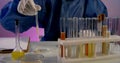 Close-up of a table with test tubes in a stand. a person in blue protective clothing and white gloves drips from a