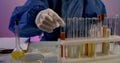 Close-up of a table with test tubes in a stand. a person in blue protective clothing and white gloves examines the