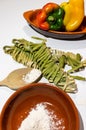 Close up tagliatelle pasta with pesto and flour, yellow and red peppers and wooden spoon  white background Royalty Free Stock Photo