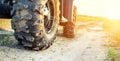 Close-up tail view of ATV quad bike on dirt country road at evening sunset time. Dirty wheel of AWD all-terrain vehicle. Travel