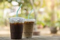 Close up of take away plastic cup of iced black coffee Americano and iced coffee latte on wooden table in garden with copy sapce Royalty Free Stock Photo