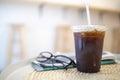 Close up of take away plastic cup of iced black coffee Americano on round table with news paper and reading glasses in the Royalty Free Stock Photo
