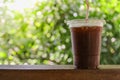 Close up of take away plastic cup of iced black coffee Americano under sunlight on wooden table in garden with green nature Royalty Free Stock Photo