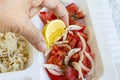 Hand squeezes lemon to tomato salad on portion food tray,