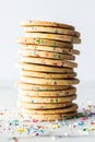 Close up of a stack of homemade sprinkle sugar cookies against a light background with sprinkles scattered around.
