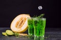 Close-up of a tarragon drink. A glass of green alcoholic lime cocktail. Cold drink and sweet cut melon on a black background. Royalty Free Stock Photo