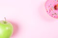 Close-up of tasty donuts and fresh green apple on pink background suggesting healthy food concept Royalty Free Stock Photo