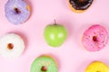 Close-up of tasty donuts and fresh green apple on pink background suggesting healthy food concept Royalty Free Stock Photo