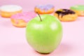 Close-up of tasty donuts and fresh green apple on pink background suggesting healthy food concept Royalty Free Stock Photo