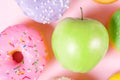 Close-up of tasty donuts and fresh green apple on pink background suggesting healthy food concept Royalty Free Stock Photo