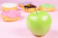 Close-up of tasty donuts and fresh green apple on pink background suggesting healthy food concept Royalty Free Stock Photo