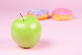 Close-up of tasty donuts and fresh green apple on pink background suggesting healthy food concept Royalty Free Stock Photo