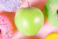 Close-up of tasty donuts and fresh green apple on pink background suggesting healthy food concept Royalty Free Stock Photo