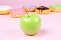 Close-up of tasty donuts and fresh green apple on pink background suggesting healthy food concept Royalty Free Stock Photo