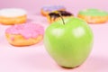 Close-up of tasty donuts and fresh green apple on pink background suggesting healthy food concept Royalty Free Stock Photo