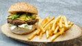 Tasty hamburger with cheddar cheese, hot chili pepper, french fries, american salad and cucumber pickle on a natural wooden tray