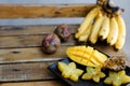 Close up tasty mango and carambola on plate near bananas on wooden table.