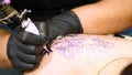 Close-up, in a tattoo salon , a specialist is doing a tattoo on woman`s back, black paint floral ornament. a man works