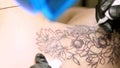 Close-up, in a tattoo salon , a specialist is doing a tattoo on woman`s back, black paint floral ornament. a man works