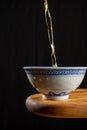 Close-up of tea falling into china cup, on wooden table, black background, vertical, Royalty Free Stock Photo