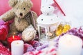 A close-up of a teddy bear with Christmas candles on a cozy checkered plaid outdoors next to a red gift box sprinkled