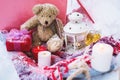 A close-up of a teddy bear with Christmas candles on a cozy checkered plaid outdoors next to a red gift box sprinkled