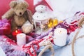 A close-up of a teddy bear with Christmas candles on a cozy checkered plaid outdoors next to a red gift box sprinkled