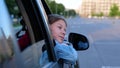 Close up of teen kid looking outdoor on city street pulls her face and hand out of car window in good mood. Beautiful Royalty Free Stock Photo